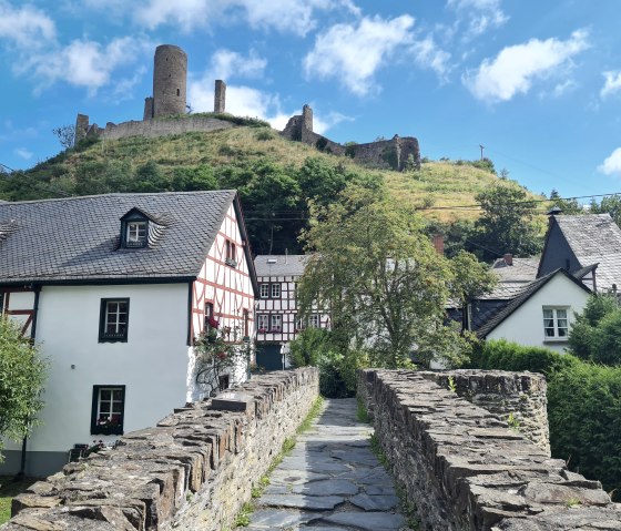 Fachwerkhäuser und eine alte Steinmauer führen den Blick zur Löwenburg auf einem Hügel in Monreal, unter blauem Himmel., © Svenja Schulze-Entrup Fachwerkhäuser und eine alte Steinmauer führen den Blick zur Löwenburg auf einem Hügel in Monreal, unter blauem Himmel., © Svenja Schulze-Entrup