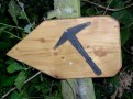 Een houten bord met een hamer van zwarte leisteen als symbool, dat is bevestigd aan een boom in het bos en dient als wegwijzer., © Svenja Schulze-Entrup Een houten bord met een hamer van zwarte leisteen als symbool, dat is bevestigd aan een boom in het bos en dient als wegwijzer., © Svenja Schulze-Entrup