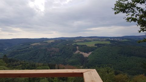 Ein schöner Ausblick auf grüne Hügel und Wälder unter einem bewölkten Himmel. Die Landschaft wirkt ruhig und einladend.