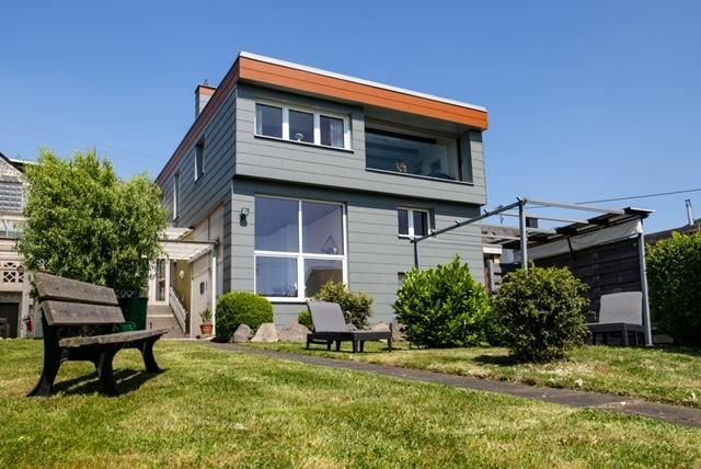 Ein modernes Haus mit großen Fenstern und einem orangefarbenen Dach. Der Garten ist gepflegt, mit Rasenflächen und bequemen Sitzgelegenheiten.