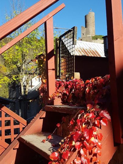A red staircase with autumn leaves leads to a building. In the background, a tower and a clear blue sky can be seen.