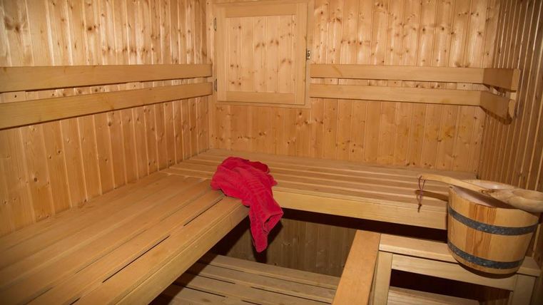 Eine gemütliche Sauna aus Holz mit Bänken und einem Eimer. Ein rotes Handtuch liegt auf einer der Bänke.
