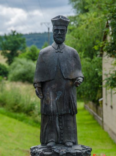 Bronzestatue eines Mannes in traditioneller Kleidung auf einem Sockel im Freien.