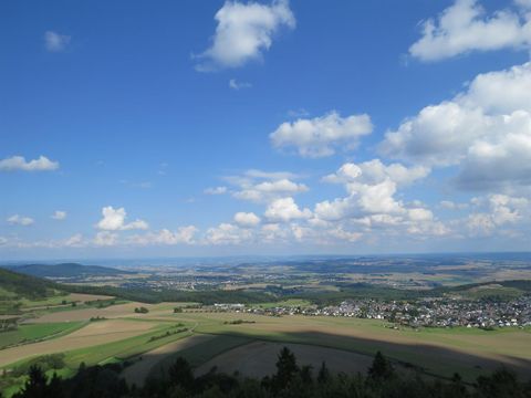 A vast landscape with hills and fields under a clear sky. White clouds drift across the scene, giving the image a tranquil atmosphere.