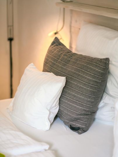 A cozy bed with two pillows, one white and one gray striped. Soft light creates a relaxed atmosphere.
