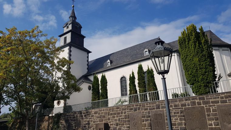Eine alte Kirche mit einem hohen Turm und schönen Bäumen im Vordergrund. Die klare, blaue Himmel verleiht der Szene eine ruhige Atmosphäre.