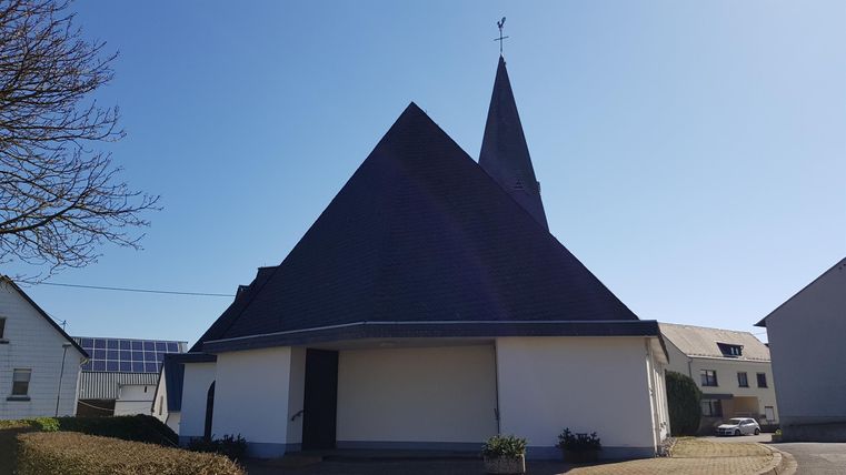 Eine moderne Kirche mit einem auffälligen, dreieckigen Dach und einem hohen Kirchturm. Der Himmel ist klar und blau.