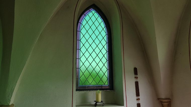 A colorful stained glass window with a gothic design. In the foreground, there is a candle on the windowsill.