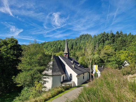 Eine charmante Kirche mit einem hohen Turm, umgeben von üppigem Grün. Der klare Himmel verleiht der Szene eine friedliche Atmosphäre.