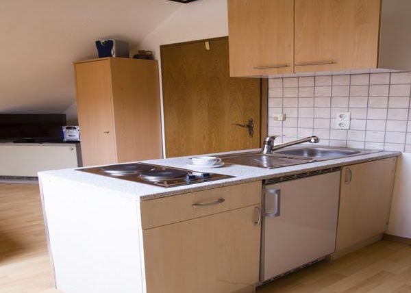 Eine kleine Küche mit Holzschränken und einem beigen Boden. Die Kücheneinheit hat eine Spüle und eine Kochplatte.
