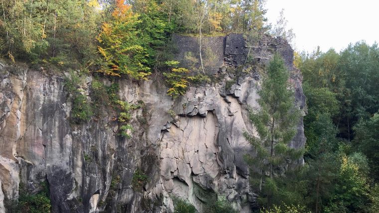 Eine steile Felswand mit bewaldeten Bereichen und bunter Herbstvegetation. Die natürliche Landschaft zeigt eine Mischung aus Felsen und Bäumen.