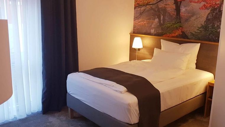 A cozy bedroom with a single bed and modern furnishings. On the wall hangs a picture of a tree in autumn colors.