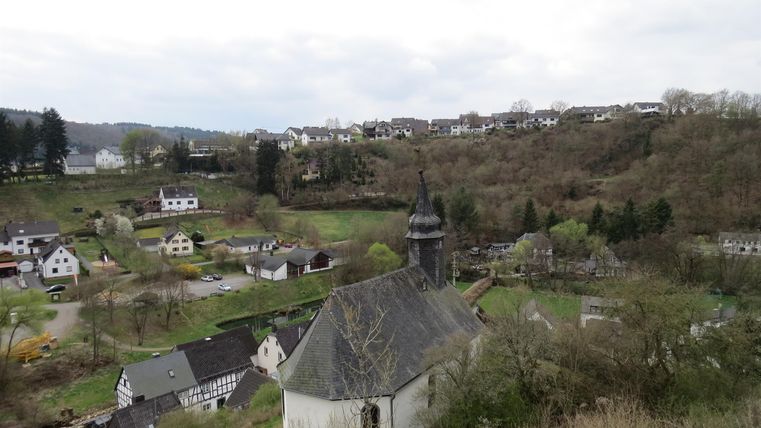 A picturesque landscape with a small village and a church. The surroundings are hilly and green, under a cloudy sky.