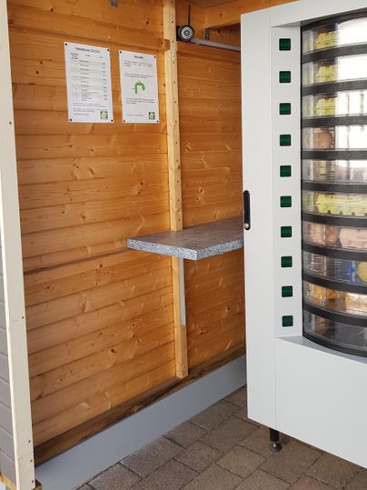 A vending machine in a wooden room. Two information sheets are hanging on the wall.