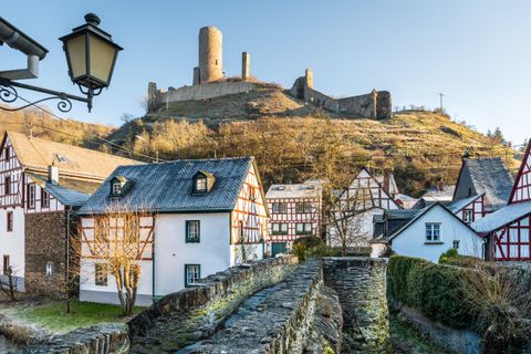 A picturesque landscape with charming houses in the foreground and an old castle on a hill in the background. The scene is illuminated by the warm light of a clear sky.