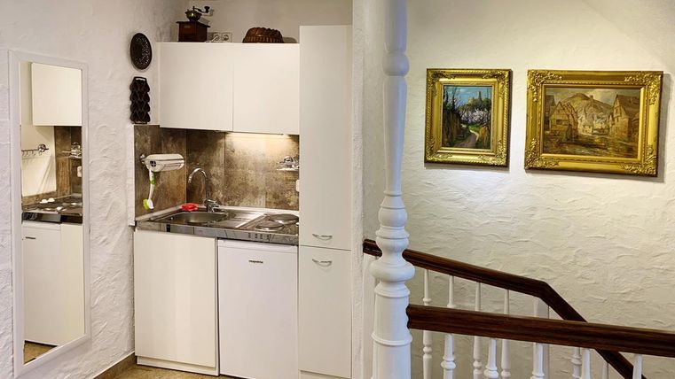 Eine kleine, helle Küche mit modernen Geräten und einem Spiegel. An der Wand hängen zwei dekorative Bilder, und die Treppe führt nach oben.