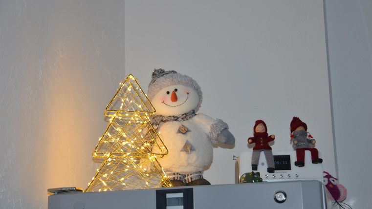 A decorated refrigerator with a bright, three-dimensional Christmas tree and a cute snowman. Next to it are two small figures in festive clothing.