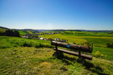 Bank auf Hügel mit Weitsicht über Felder, einen Ort und blauem Himmel