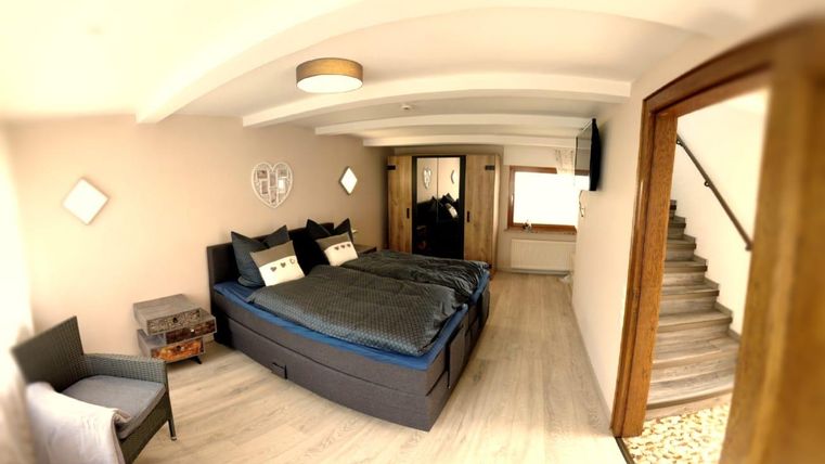 Ein gemütliches Schlafzimmer mit zwei Betten und einer modernen Einrichtung. Es gibt einen Stuhl in der Ecke und eine Treppe im Hintergrund.