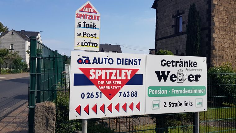 Ein Schild mit Informationen zu einem Auto-Dienst und einer Pension. Es zeigt auch Hinweise auf Tankstelle, Post und Lotto.