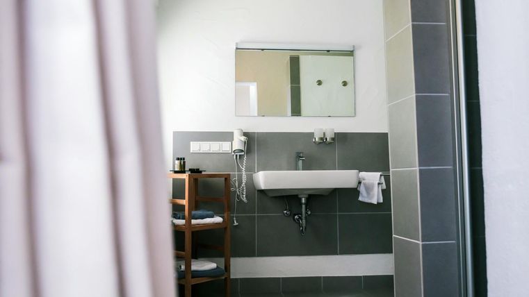 A modern bathroom with a sink and a large mirror. Next to the sink is a shelf with towels.