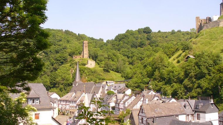 Eine malerische Stadt mit Fachwerkhäusern liegt in einem grünen Tal. Im Hintergrund ragt ein alter Turm über die sanften Hügel.