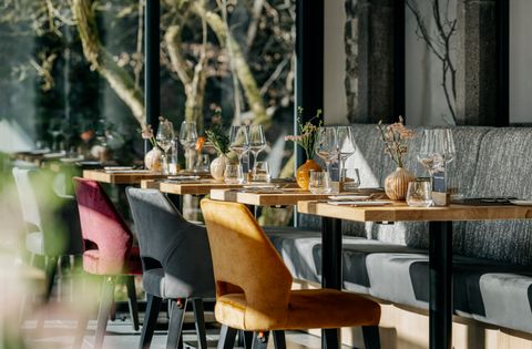 A modern restaurant with elegantly set tables and colorful chairs. Large windows let in plenty of daylight and create an inviting atmosphere.