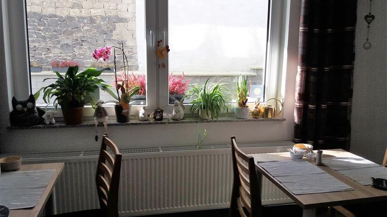 A cozy room with two tables and chairs. Many plants and decorations are on the windowsill.