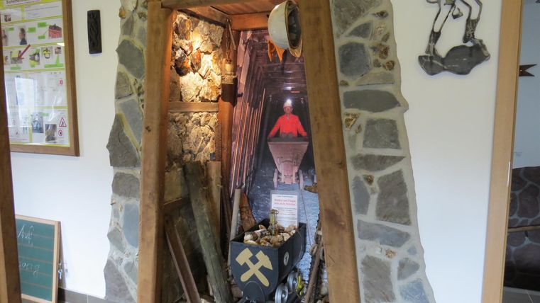 Eine rustikale Nische mit verschiedenen Bergbau-Elementen, darunter Werkzeuge und eine Laterne. Die Steine und Holzverkleidung vermitteln ein traditionelles, handwerkliches Ambiente.