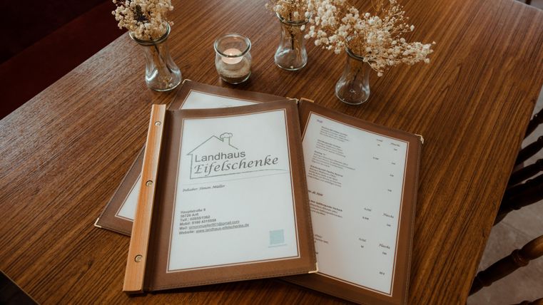 Ein Tisch mit einer Speisekarte in einem rustikalen Restaurant. Vasen mit getrockneten Blumen sorgen für eine gemütliche Atmosphäre.