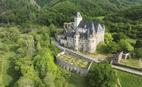 An impressive castle with towers and a garden surrounded by forest.