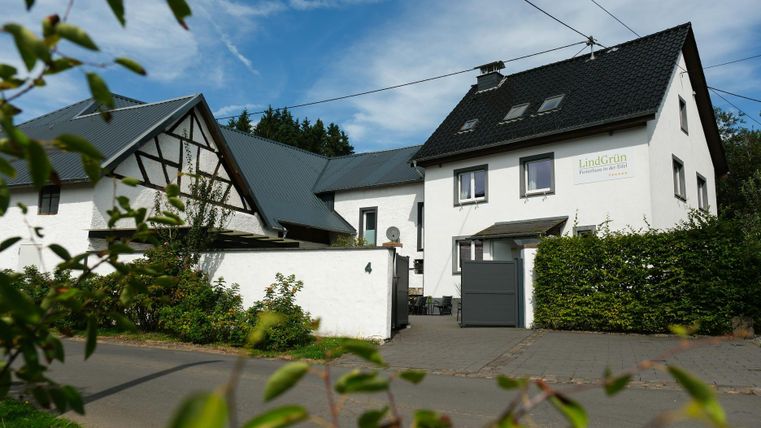 A modern house with a white paint and a black roof.
Surrounded by green bushes and a clear sky.