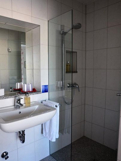 A modern bathroom with a glass shower and a sink. The walls are tiled in light colors and there are towels and toiletries.