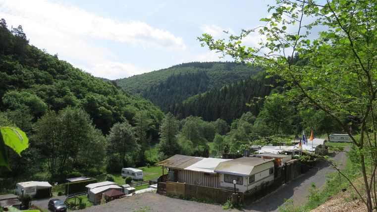Eine ruhige Landschaft mit einem Campingplatz in einem grünen Tal. Umgeben von Hügeln und Bäumen bietet der Platz eine naturnahe Atmosphäre.