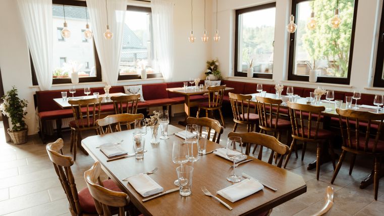 Ein gemütliches Restaurant mit Holzstühlen und Tischen. Große Fenster sorgen für viel natürliches Licht und eine angenehme Atmosphäre.