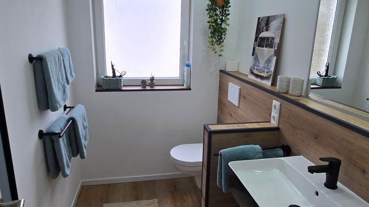 Ein modernes Badezimmer mit Holzdekoren und klaren Linien. Es bietet eine elegante Waschgelegenheit und dekorative Pflanzen.