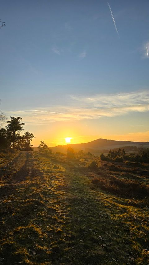 Ein schöner Sonnenuntergang über einer hügeligen Landschaft. Der Himmel ist klar und die Farben leuchten warm.