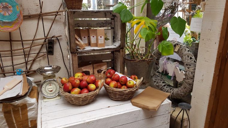 A small market stall with baskets full of fresh apples. In the background, there are plants and lovingly decorated items.