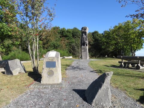 A memorial featuring a statue and commemorative plaques in a park with trees and a picnic table.