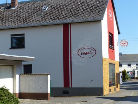 Ein zweigeschossiges Gebäude mit einer weißen und roten Fassade. An der Wand ist das Schild "Engels" angebracht.