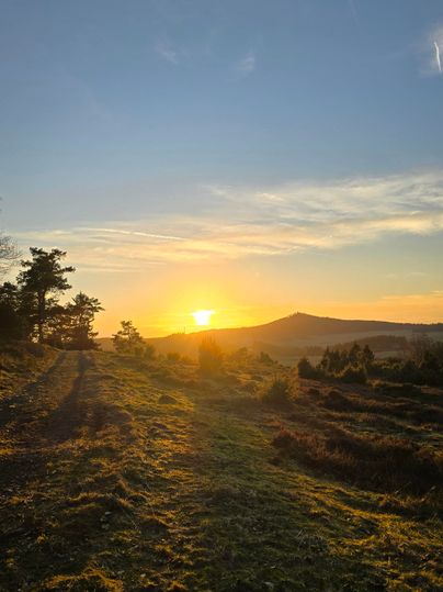 Ein schöner Sonnenuntergang über einer hügeligen Landschaft. Der Himmel ist klar und die Farben leuchten warm.