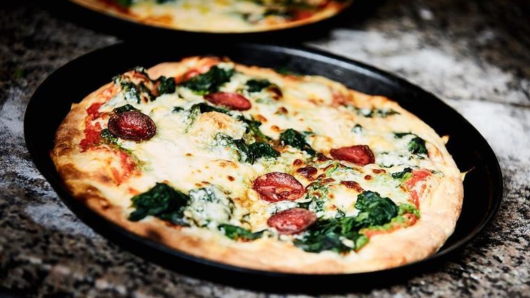 Eine köstliche Pizza mit Spinat und Wurstscheiben. Der Käse ist geschmolzen und goldbraun.