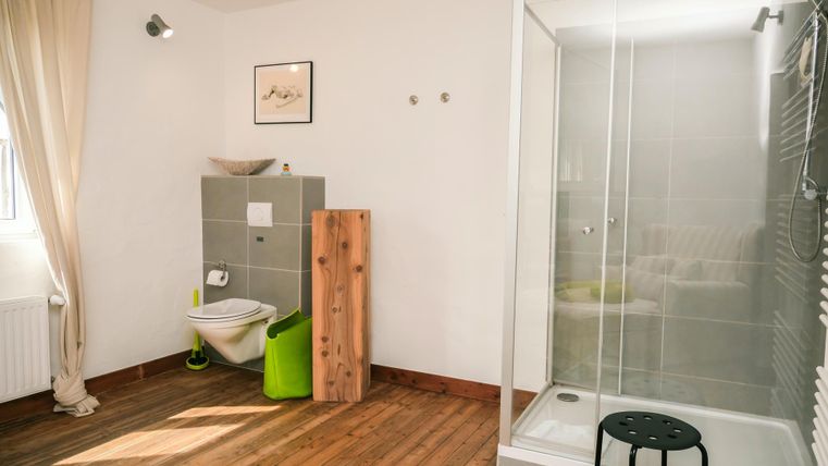A modern bathroom with a shower and a minimalist design. The floor is wooden and there is a bright color palette.