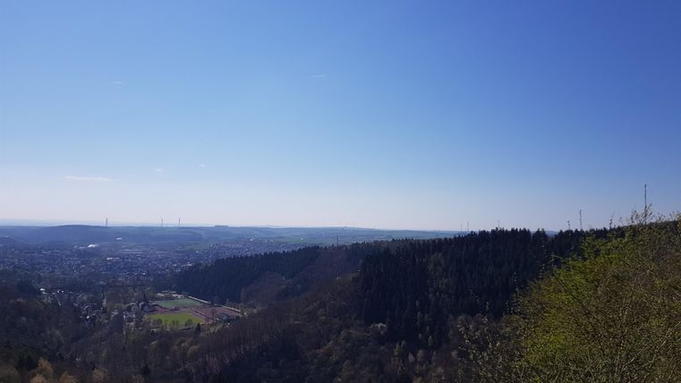 Eine weite Landschaft mit Hügeln und einem klaren blauen Himmel. Der Blick reicht über das grüne Tal bis in die Ferne.