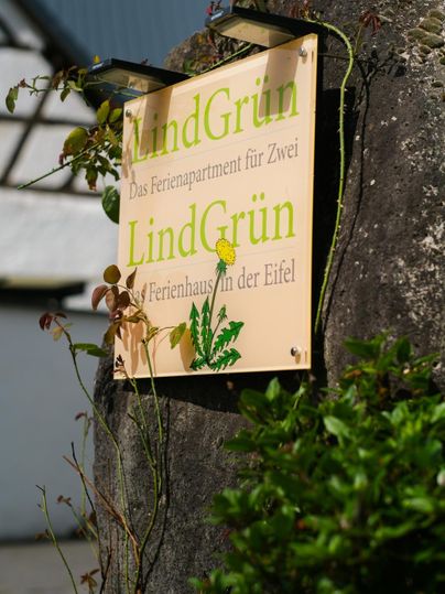 A sign with the inscription "LindGrün" indicates a holiday apartment. It features green lettering and is surrounded by plants.