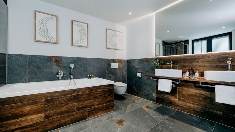 Ein modernes Badezimmer mit einer Badewanne und zwei Waschbecken. Die Wände sind in neutralen Farben gehalten und es gibt dekorative Bilder.