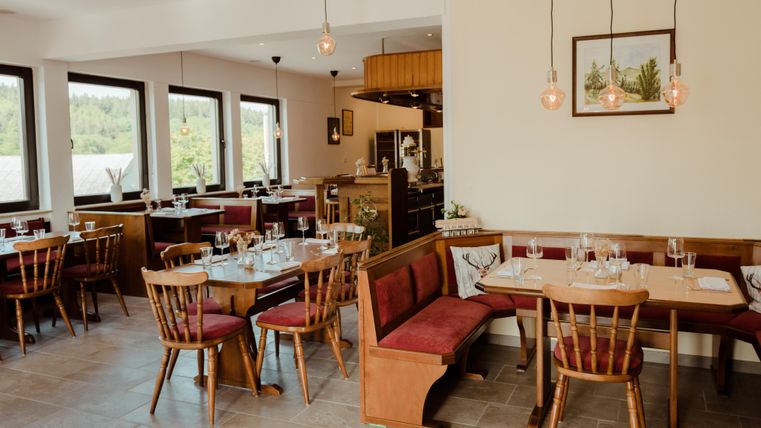Ein gemütliches Restaurant mit Holzstühlen und Tischen. Große Fenster bieten einen Blick nach draußen und eine einladende Atmosphäre.