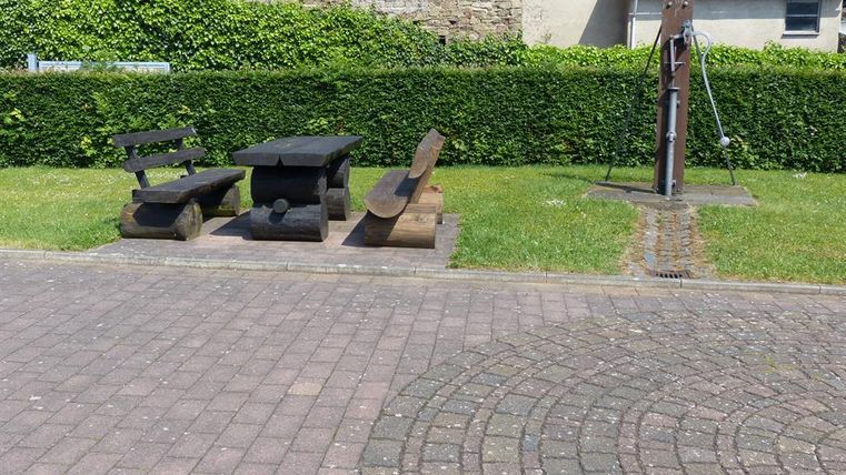 Ein entspannender Außenbereich mit Holzmöbeln und einem Brunnen. Die Umgebung ist grün und gepflegt, ideal zum Verweilen.