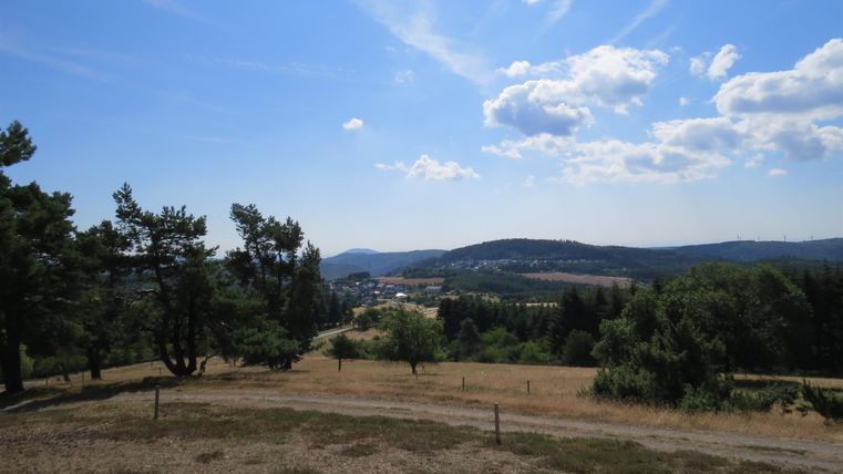A wide landscape with gentle hills and a blue sky. Countless trees and meadows shape the scenery.