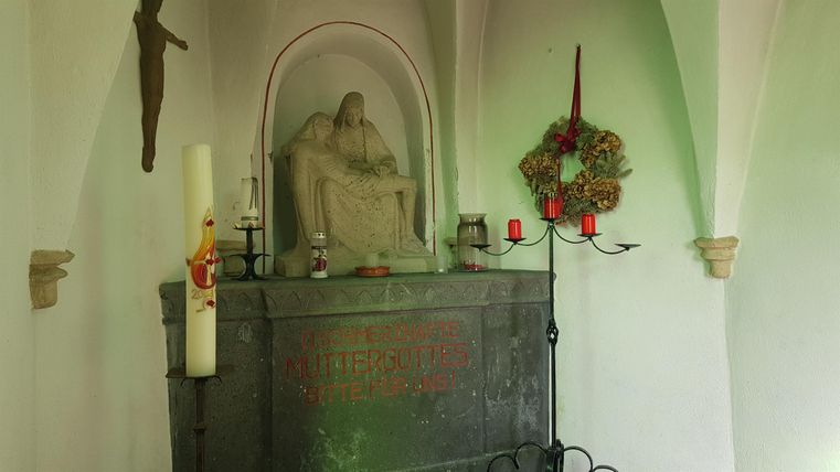 A small altar with a statue representing a seated figure. Next to it are candles and a wreath that create a tranquil atmosphere.